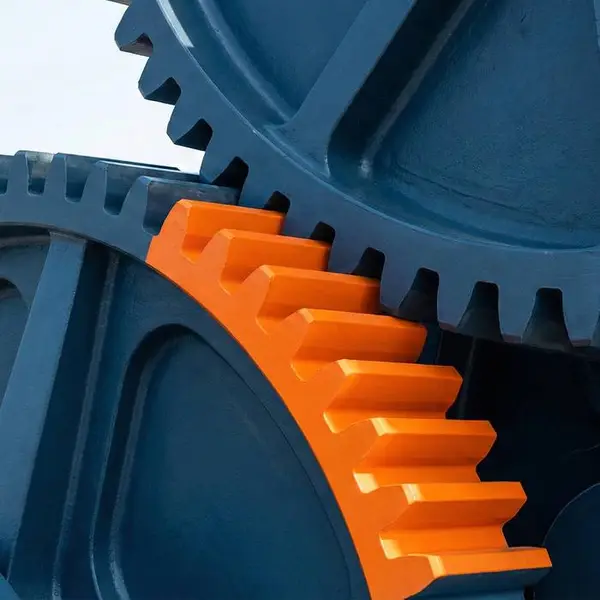 An orange gear meshing with large blue industrial gears
